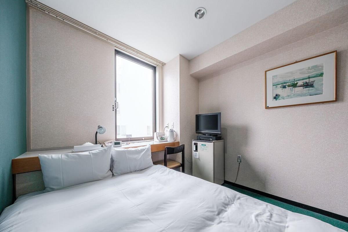 A hotel room with a large bed, a desk with a chair, a television, and a window with a view of boats.