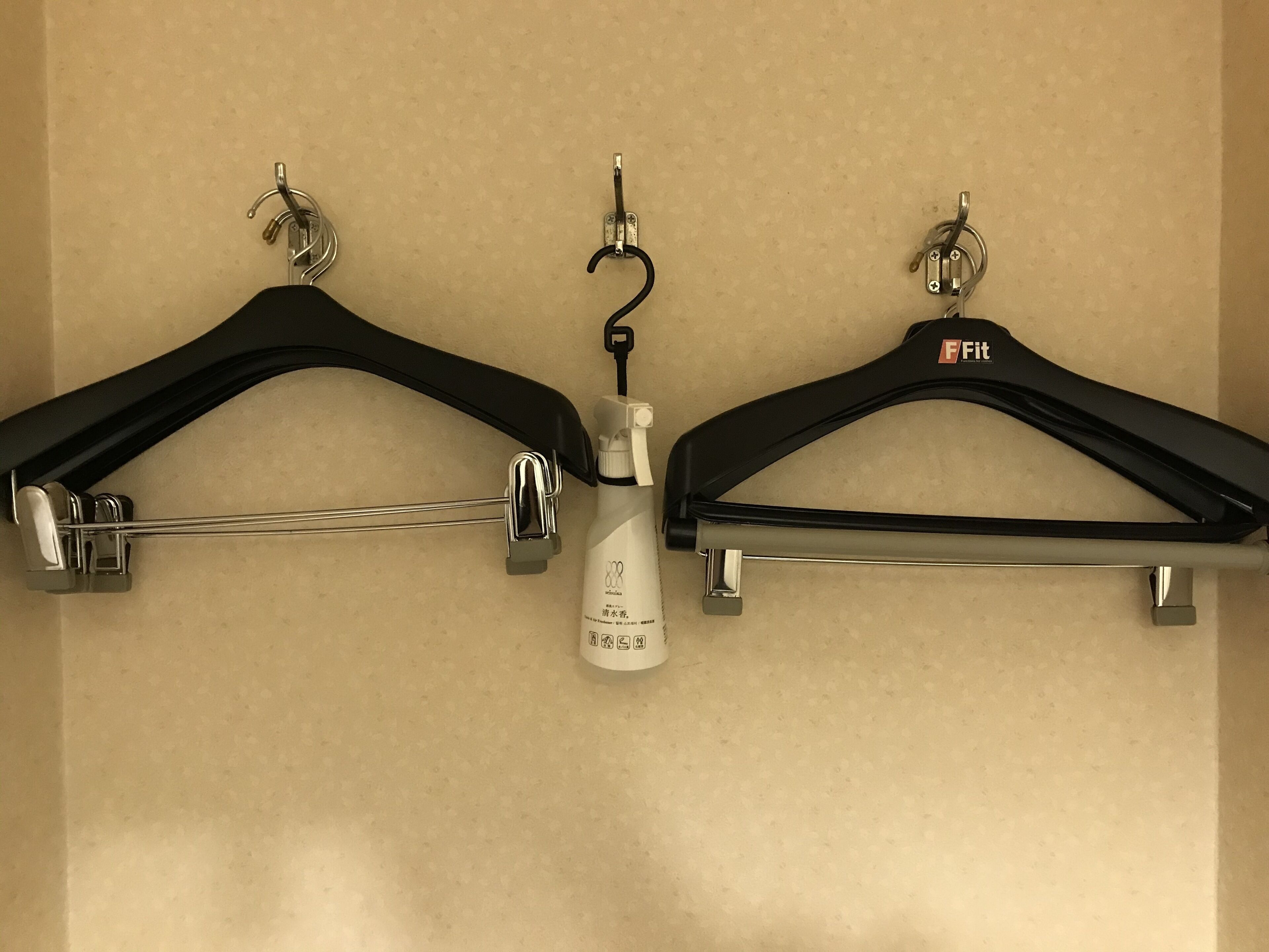 Two black hangers with metal clips on a beige wall.