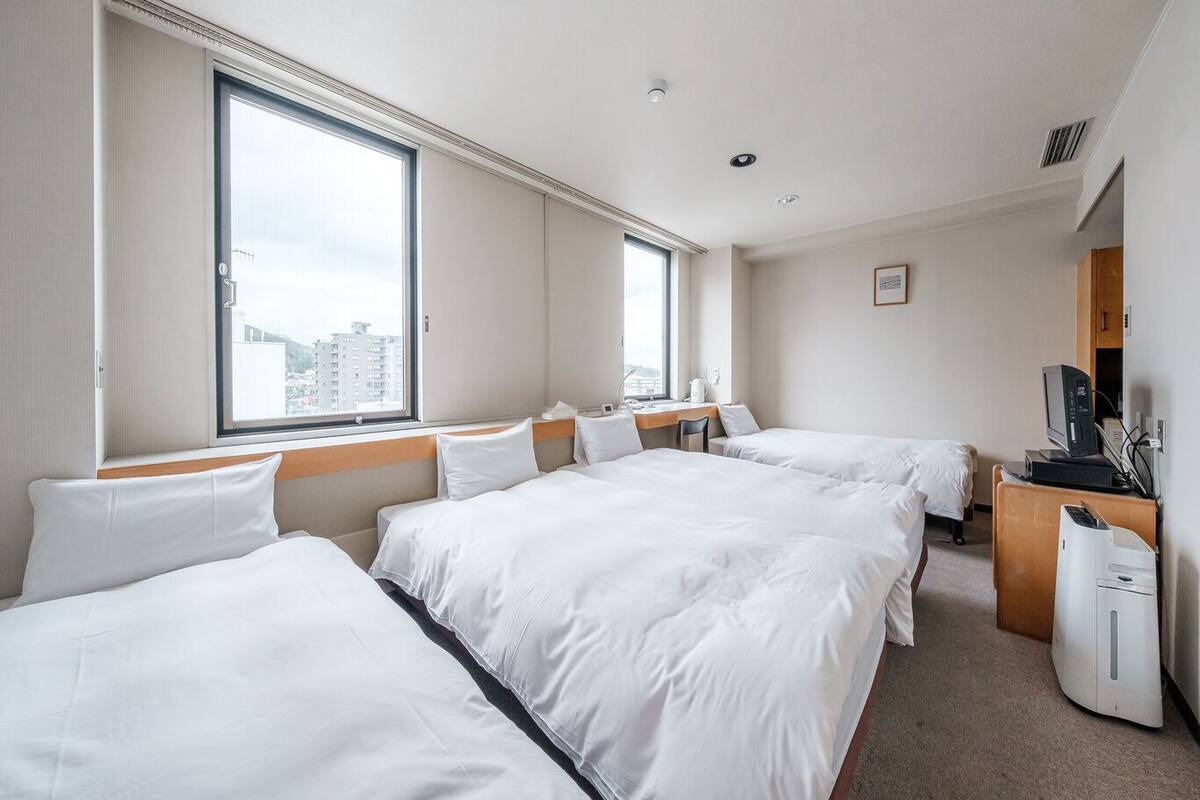 A hotel room with two beds, a desk, a TV, and a window with a city view.