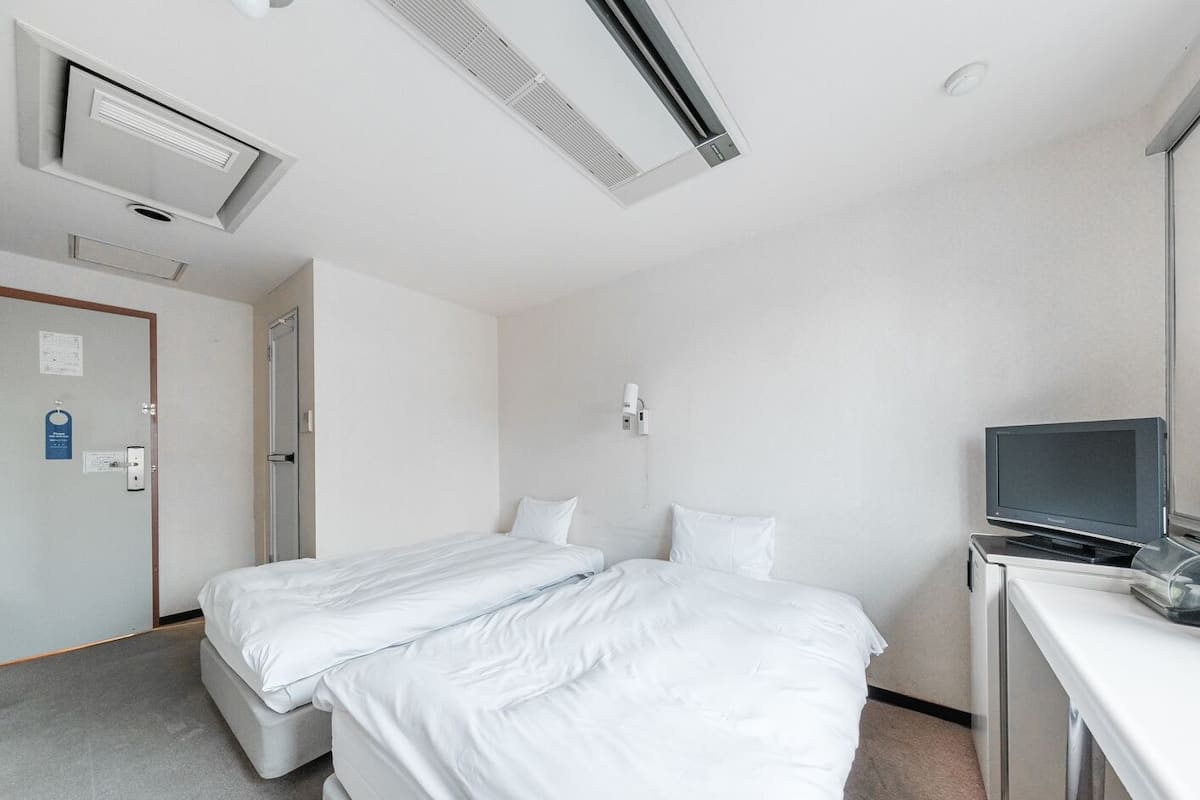 A hotel room with two beds, a desk with a television, and a wall-mounted air conditioning unit.