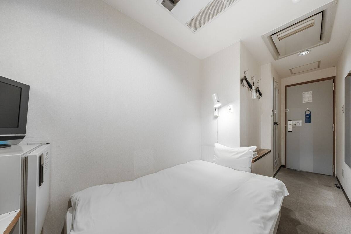 A hotel room with a bed, a TV, a desk, and a door.