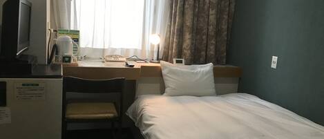 A hotel room with a bed, a desk with a chair, a television, a lamp, and a window with curtains.