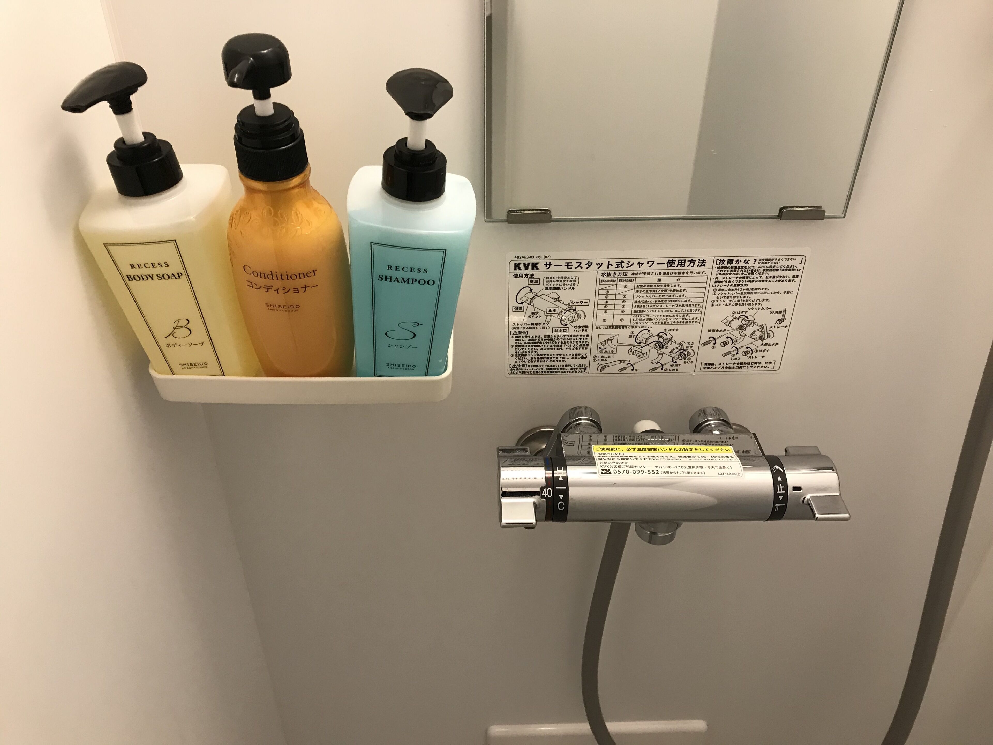 A bathroom with a shelf holding three bottles of Shiseido products, a mirror, and a towel rack with a towel.