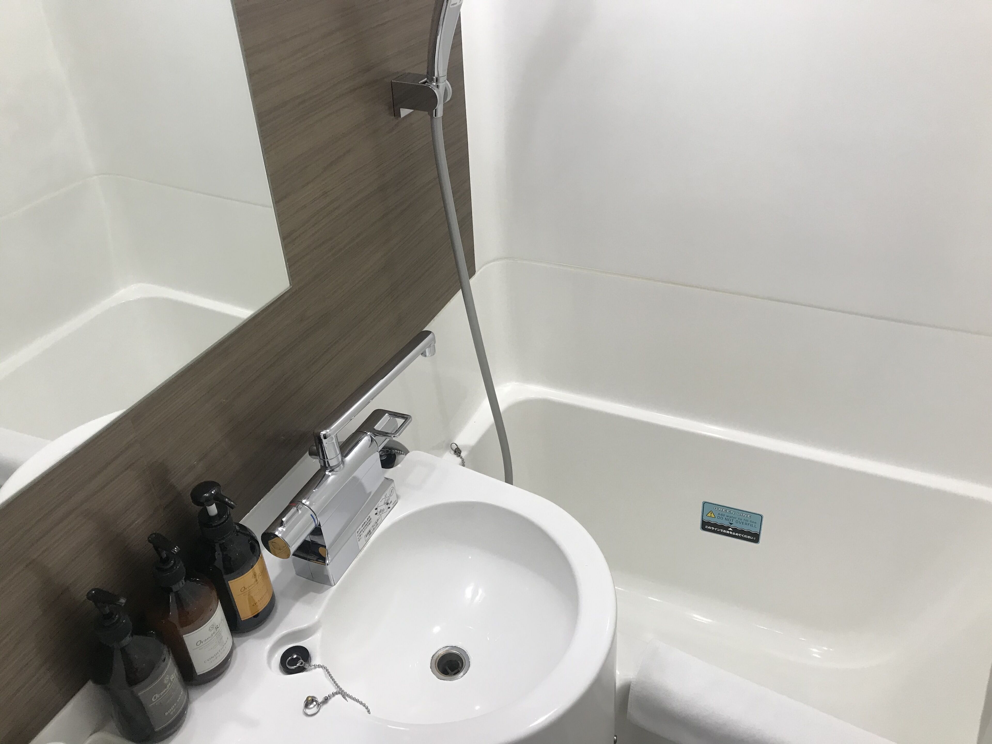 A bathroom with a white sink, a mirror, and a bathtub. There are bottles of hand soap and a soap dispenser on the sink.