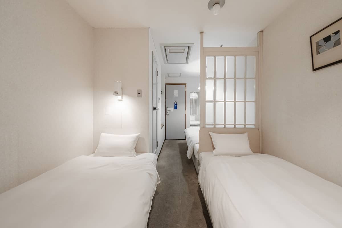 A hotel room with two single beds, a door leading to a bathroom, and a window with blinds.