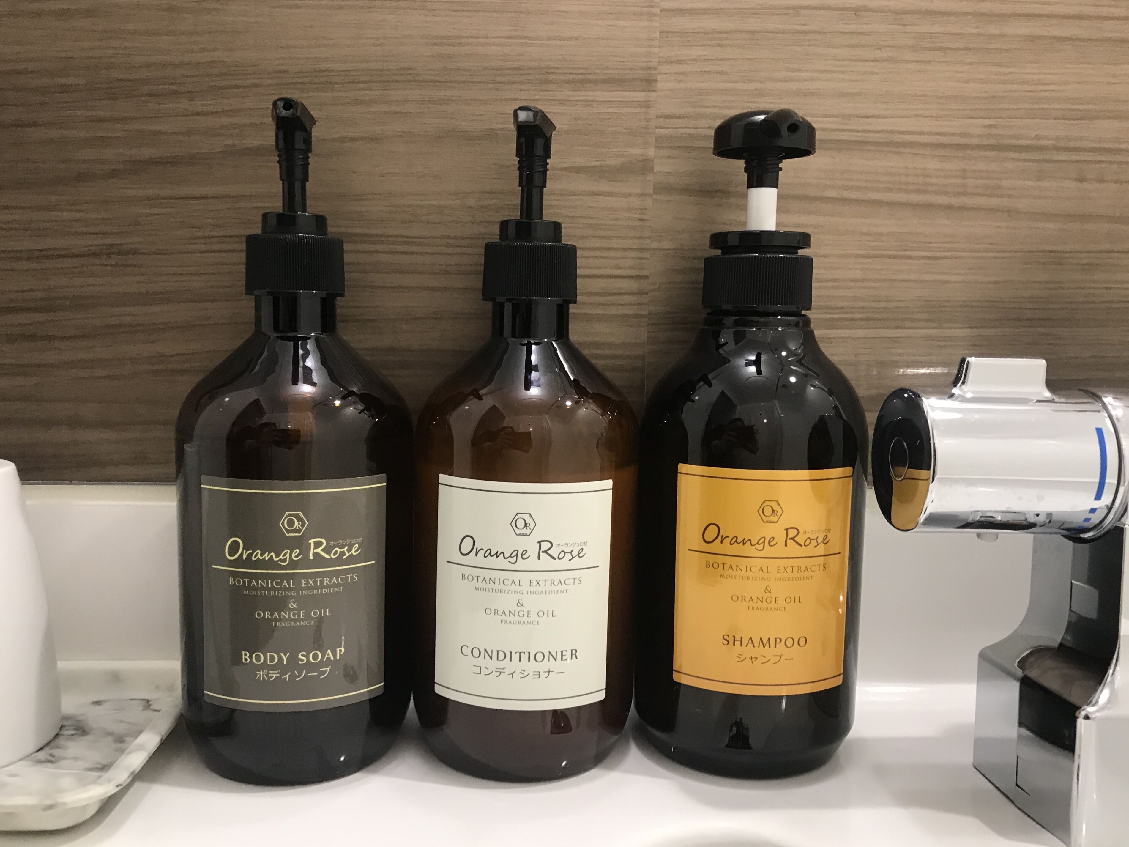 Three bottles of Orange Rose products: body soap, conditioner, and shampoo, on a bathroom counter.