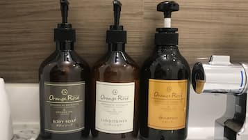 Three bottles of Orange Rose products: body soap, conditioner, and shampoo, on a bathroom counter.
