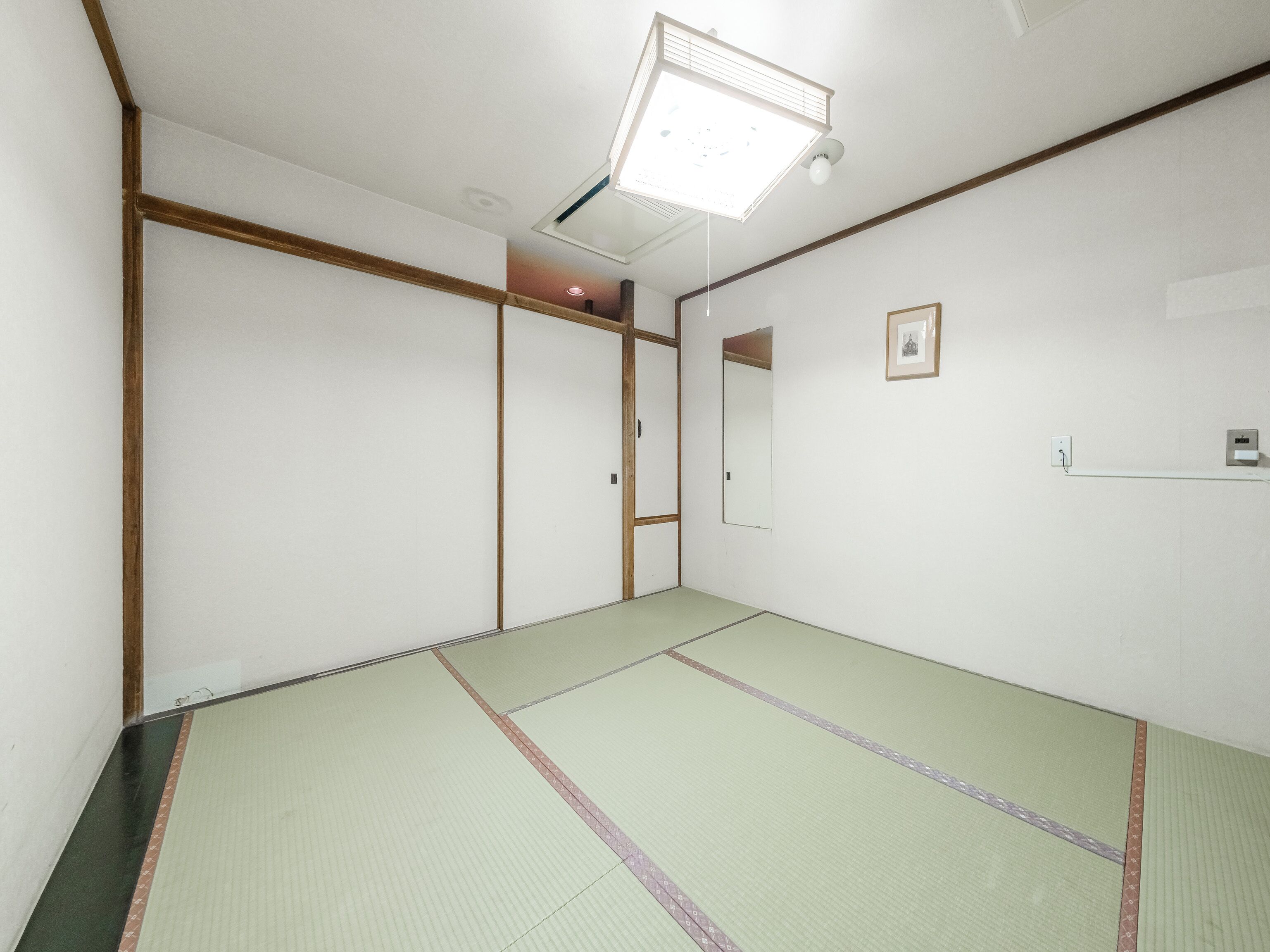 Una habitación con suelo de tatami, una lámpara de techo, un cuadro enmarcado y un enchufe.
