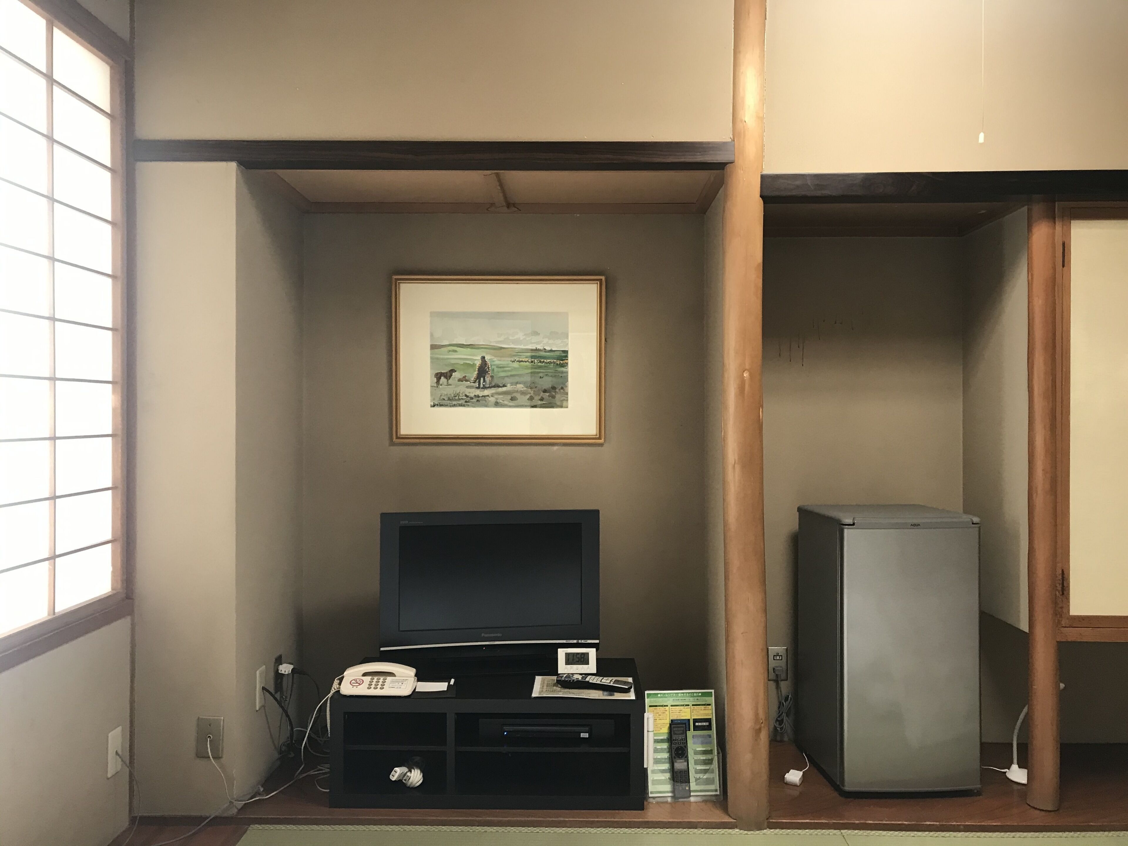 A room with a television on a stand, a framed picture on the wall, and a refrigerator.