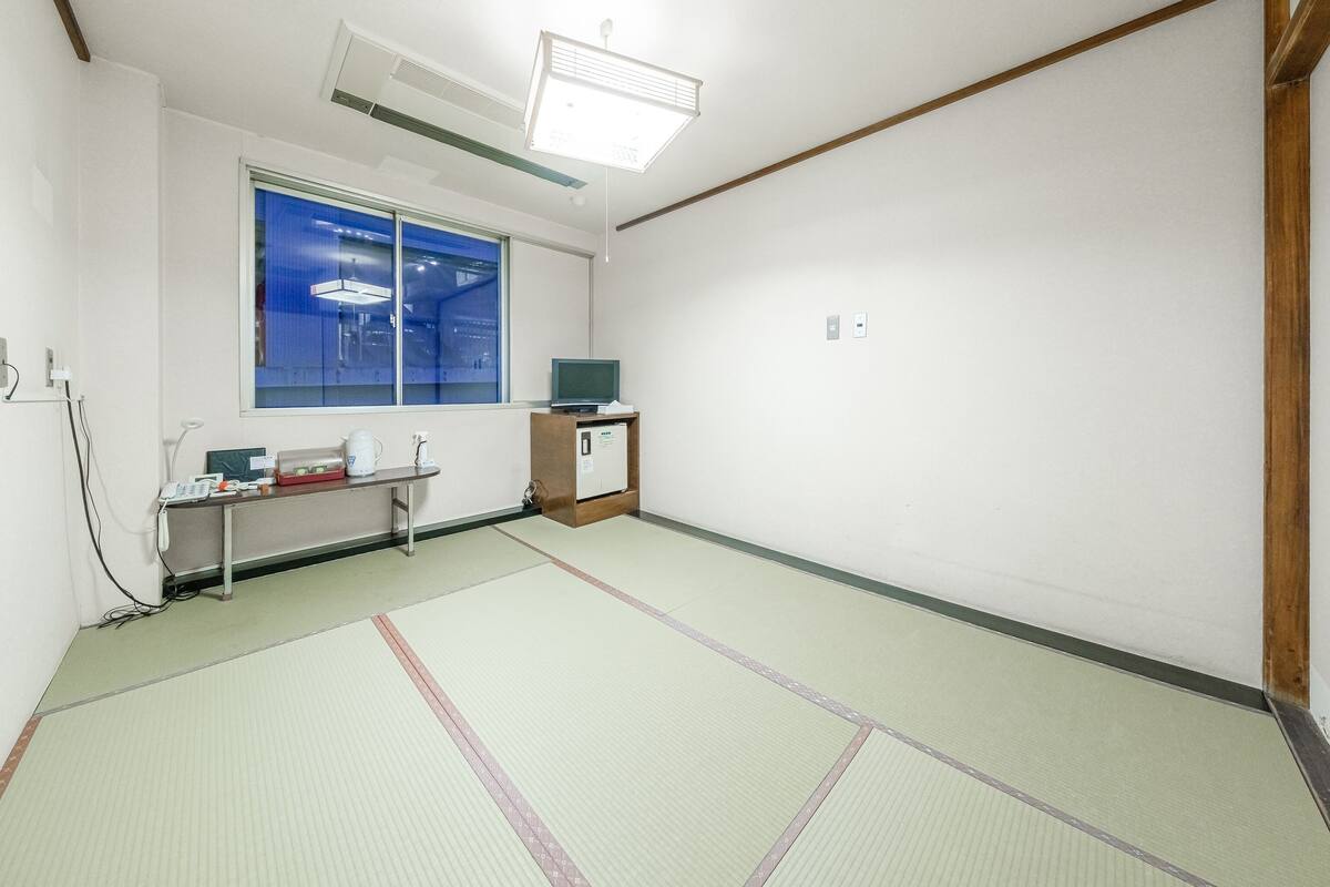 A room with tatami flooring, a window with a view, a desk with a computer, and a small cabinet.