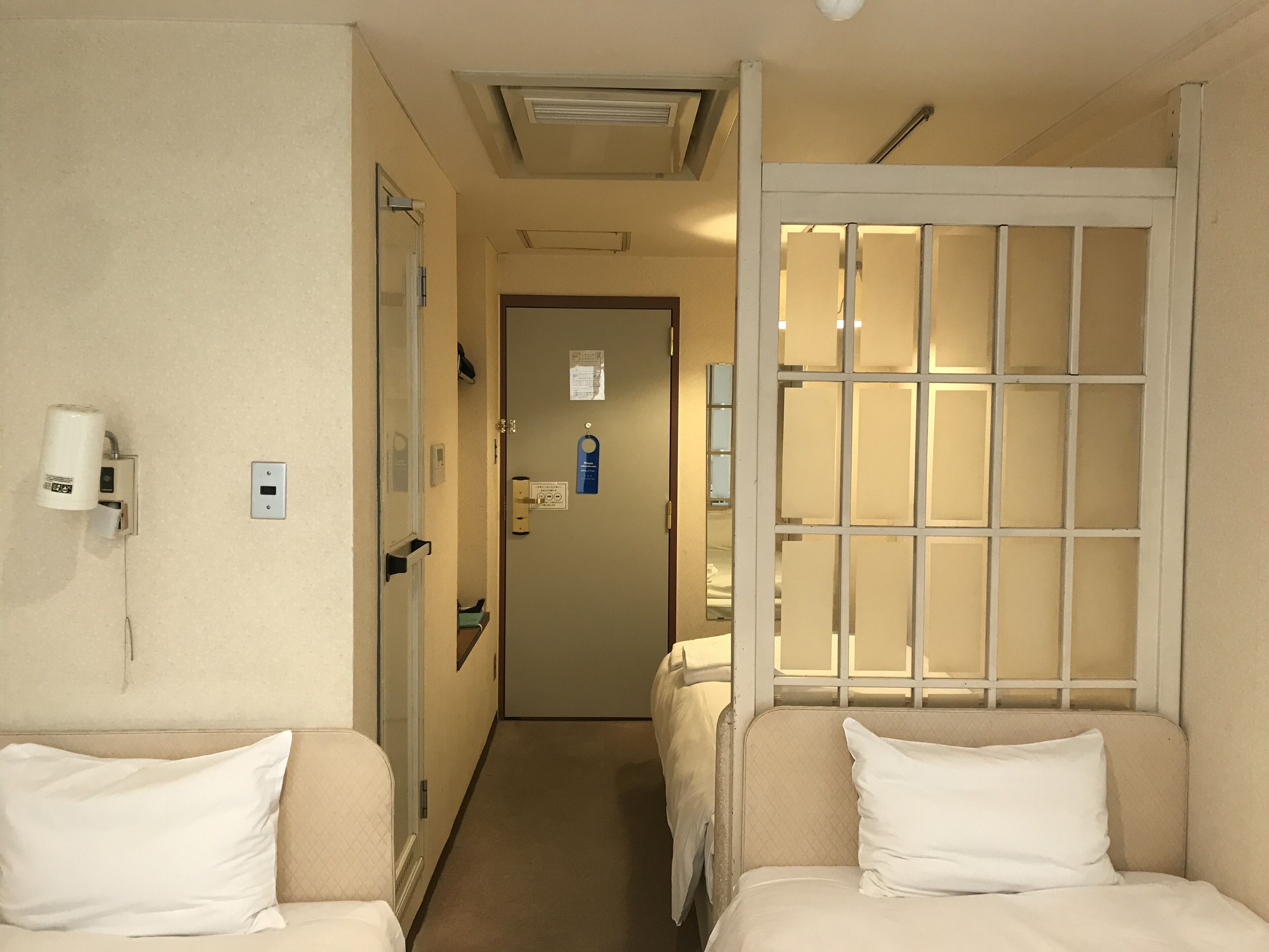 A hotel room with a bed, a small table, a chair, a nightstand, a window with a view, and a door.