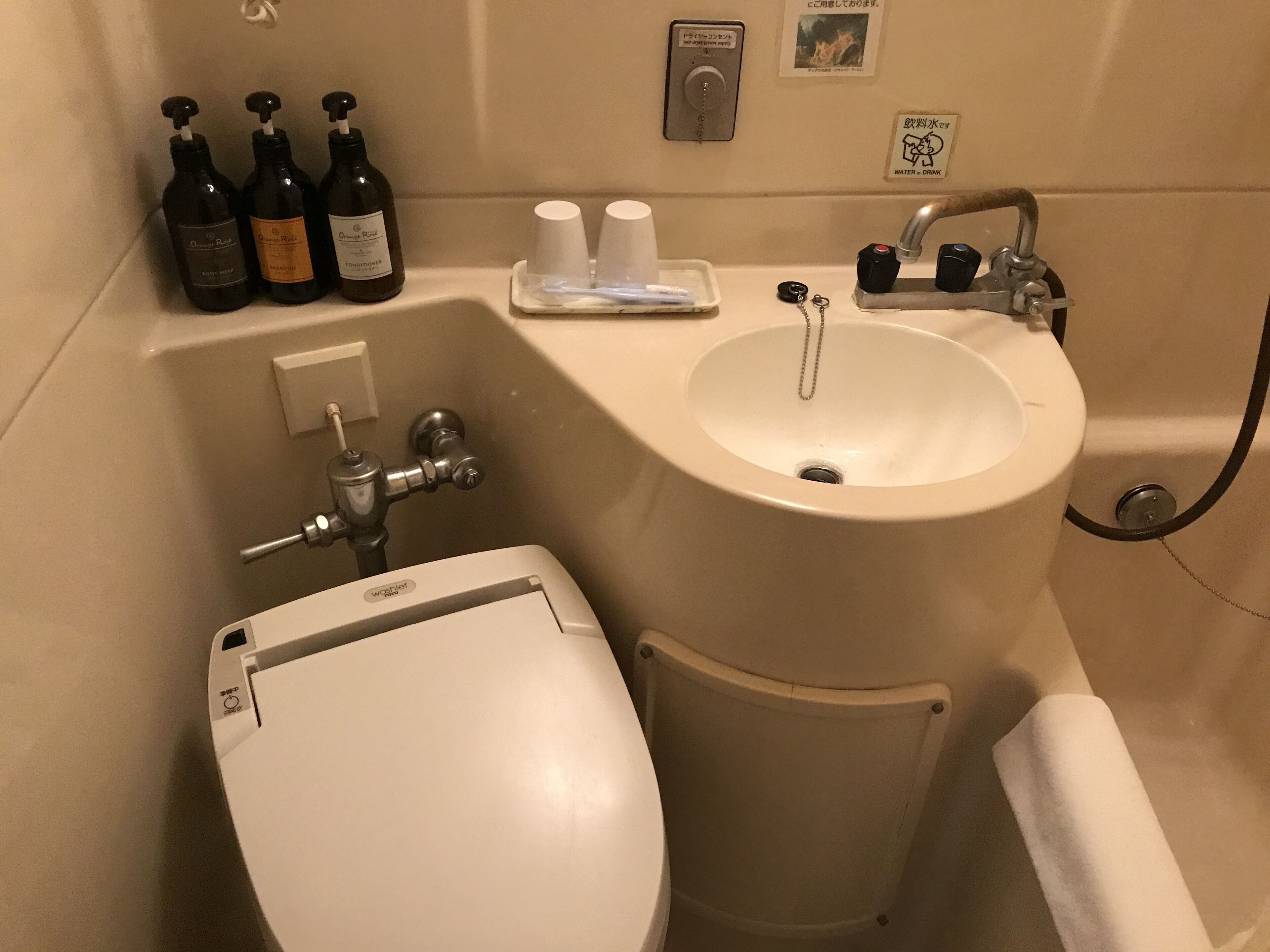 A bathroom with a toilet, sink, and shower. There are bottles of hand soap and shampoo on the counter.