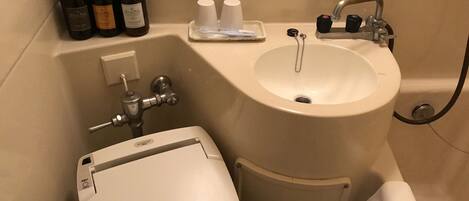 A bathroom with a toilet, sink, and shower. There are bottles of hand soap and shampoo on the counter.