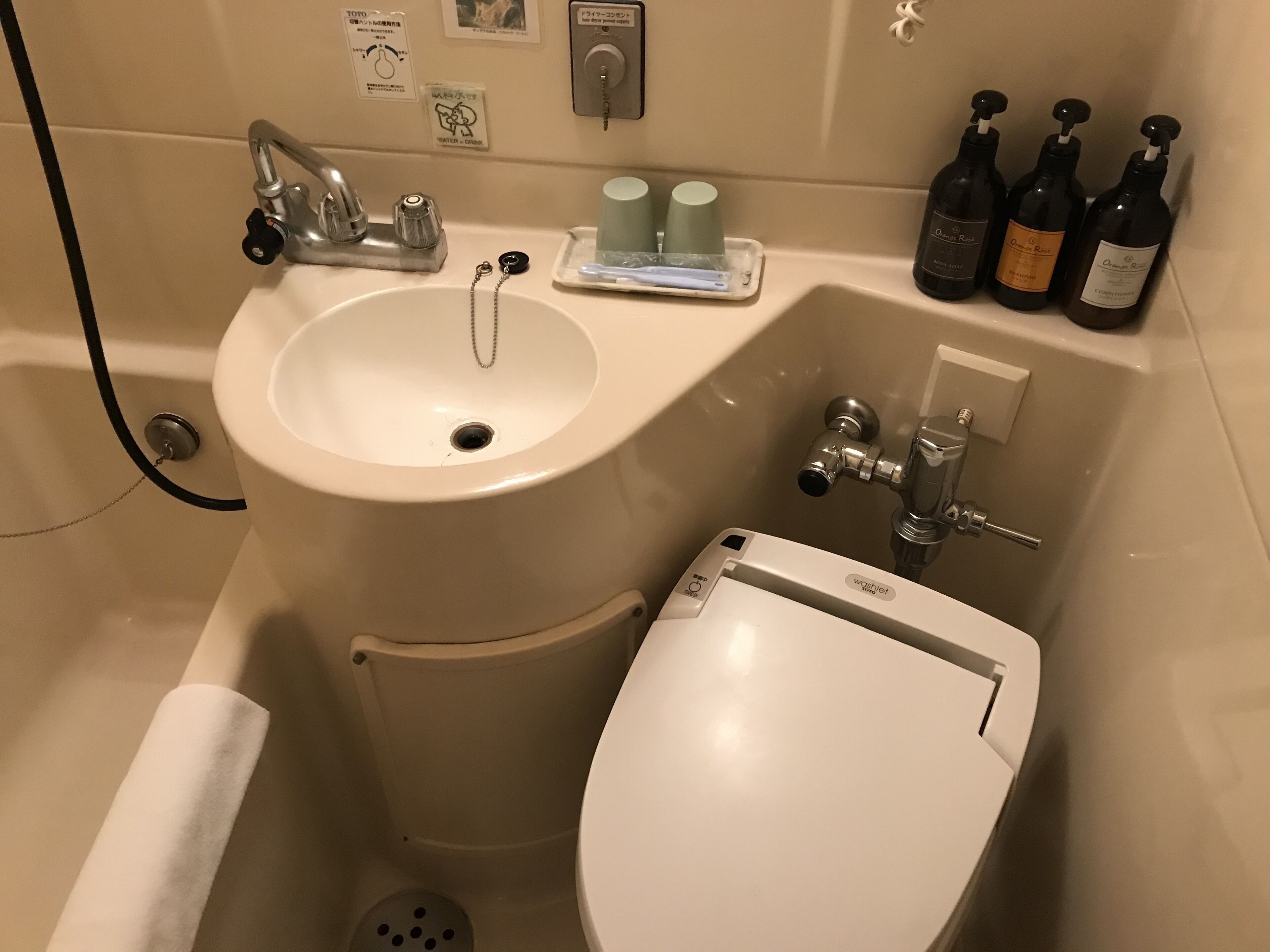 A bathroom with a sink, toilet, and a shower area. There are bottles of shampoo and conditioner on the counter.