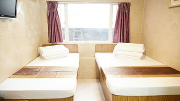 A room with two beds, a window with curtains, a television on the wall, and a wooden floor.