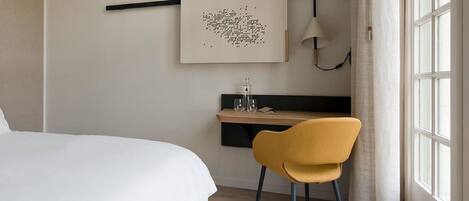 A hotel room with a bed, a desk, a chair, and a window.