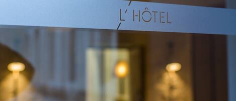 A hotel entrance with a sign reading "L'Hôtel" and a view of the street outside.