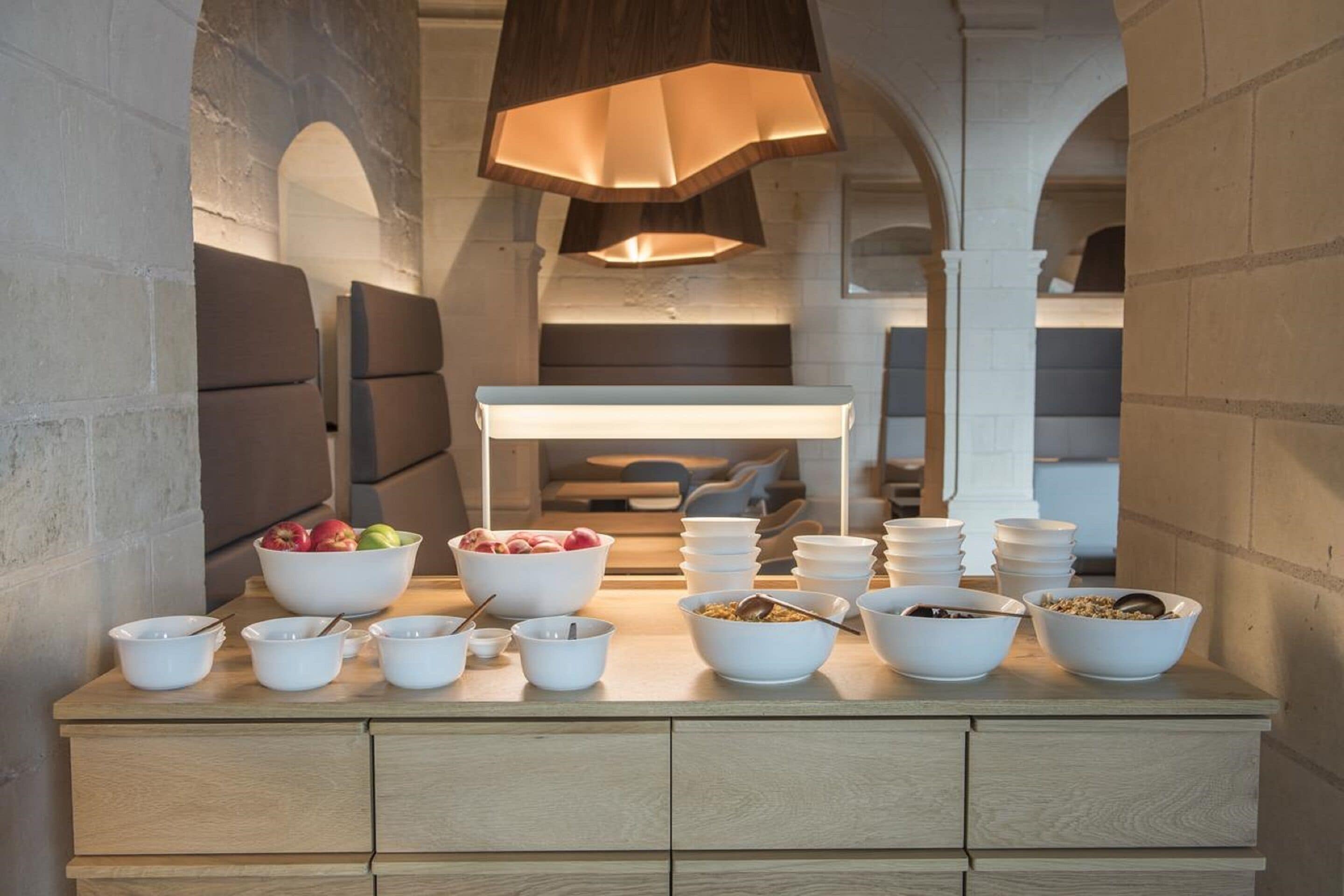 Een ontbijtbuffet met diverse schalen eten, een witte toonbank en een moderne hanglamp.