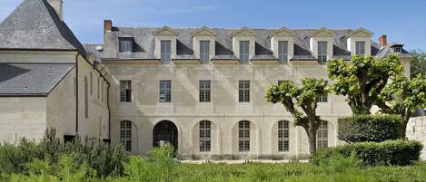 A large, historic building with a symmetrical facade, multiple windows, and a prominent tree in the foreground.