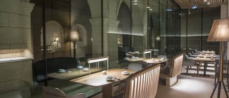 A modern restaurant with glass partitions, wooden furniture, and a ceiling with linear lighting.