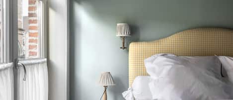 A bedroom with a checkered headboard, a bedside lamp, a patterned pillow, and a view of a brick building through a window.