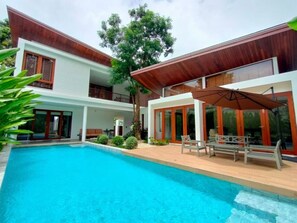 Una casa moderna de dos pisos con piscina, mobiliario exterior y ventanas amplias.