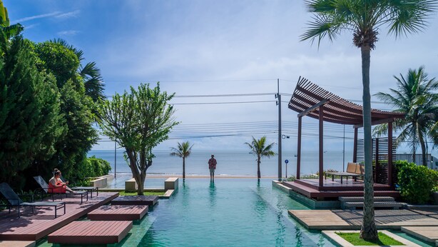 Zona de piscina con agua cristalina, muelle de madera, palmeras y vista al océano.