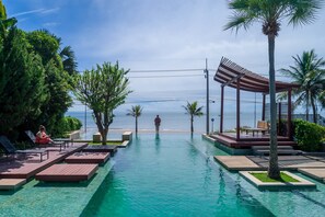 Área de piscina com água cristalina, deck de madeira, palmeiras e vista para o oceano.
