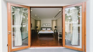Un dormitorio con una cama grande, dos mesitas de noche y vistas a palmeras a través de la puerta de cristal.