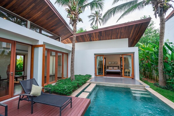 Una casa moderna con piscina, terraza de madera y exuberante vegetación.