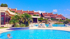 A swimming pool with lounge chairs and a building with red-tiled roofs. - Complejo Turístico Raeiros (O Grove)