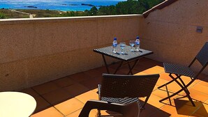 A terrace with a table and chairs, a view of the sea, and a tiled floor. - Complejo Turístico Raeiros (O Grove)