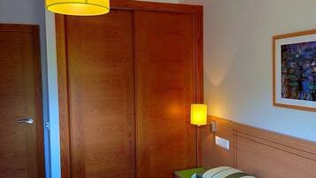 Habitación de hotel con un armario de madera, una lámpara de noche, una cama con ropa de cama a rayas y un cuadro enmarcado en la pared.