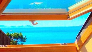 A view through a skylight of a coastal scene with a clear blue sky, a boat on the water, and a distant shoreline. - Complejo Turístico Raeiros (O Grove)