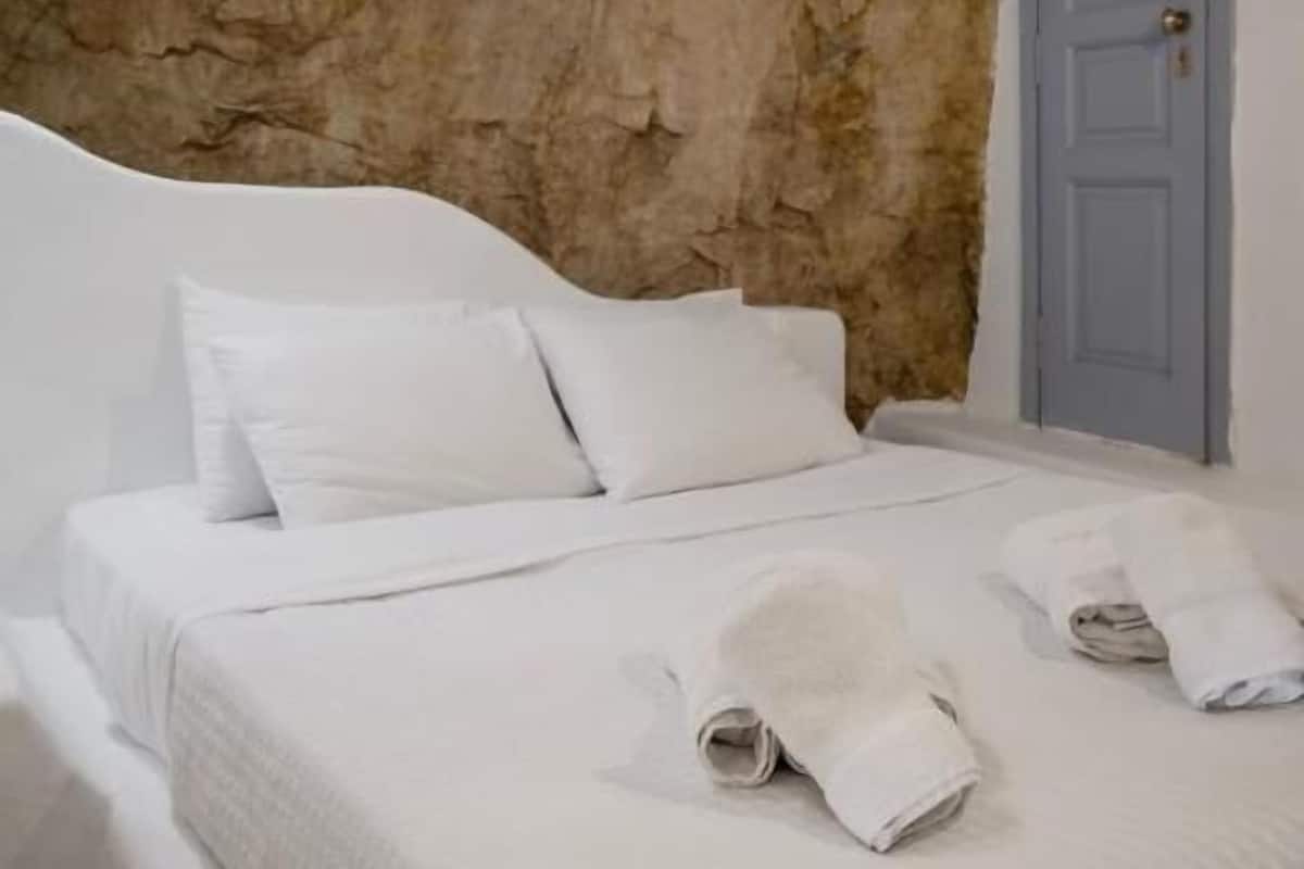 Un dormitorio con una cama blanca, pared de piedra, techo de madera y una puerta azul.