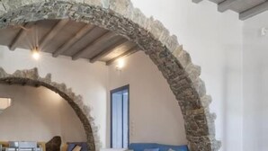 A stone archway leading to a living area with a blue sofa and a wooden table. - Nama Villas (Mykonos)
