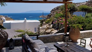 A terrace with a view of the sea, a white building, and a stone wall. - Nama Villas (Mykonos)