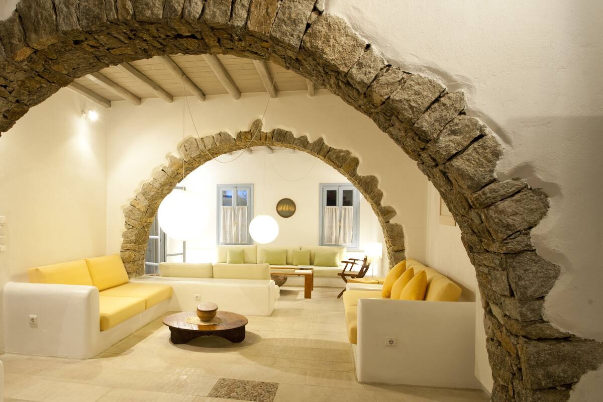 Una sala de estar con un arco de piedra, sofás blancos y una mesa de centro de madera.