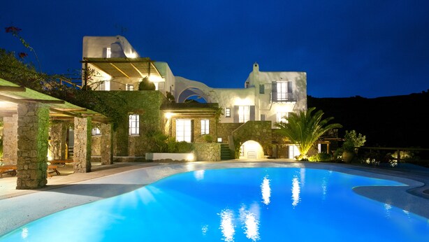 A large, modern house with a swimming pool, stone pillars, and a well-lit entrance. - Nama Villas (Mykonos)