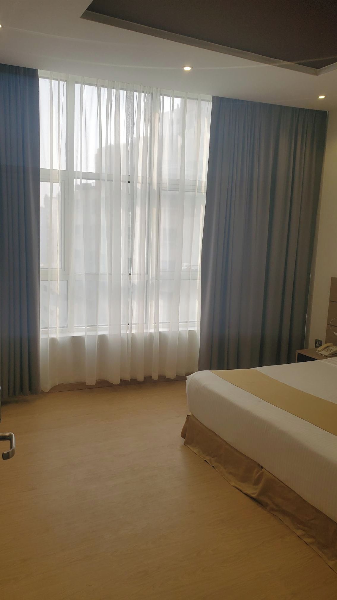 Una habitación de hotel con una cama grande, un escritorio con teléfono y cortinas translúcidas en la ventana.