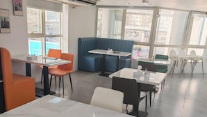 A modern restaurant with tables and chairs, a blue booth seating area, and large windows. - Aldar Hotel (Sharjah)