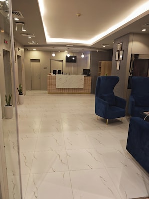 A reception area with a marble floor, a reception desk, a flat-screen TV, and blue upholstered chairs. - Aldar Hotel (Sharjah)