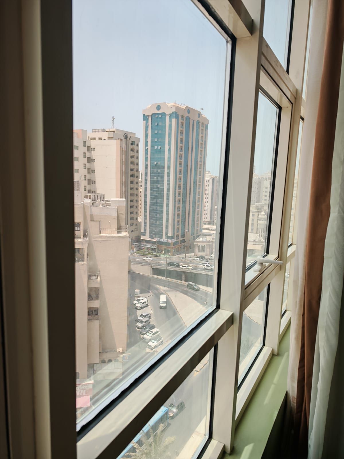 Blick aus einem Fensters mit mehreren Scheiben auf eine Skyline mit hohen Gebäuden und einer belebten Straße.