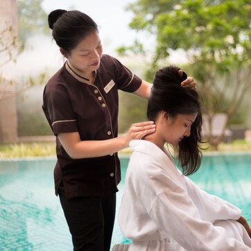 A person receiving a massage by another individual near a pool.