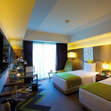 A hotel room with two beds, a desk, a chair, and a TV.