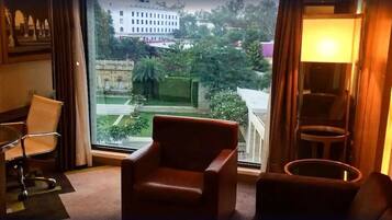 Une chambre d’hôtel avec une grande fenêtre, un fauteuil en cuir marron, une petite table ronde et une chaise de bureau blanche.