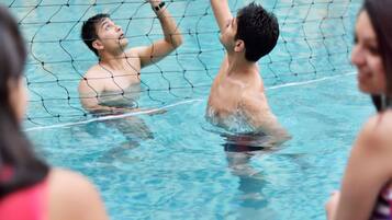 Partido de voleibol en la piscina con jugadores en el agua, una red y una mesa con bebidas.