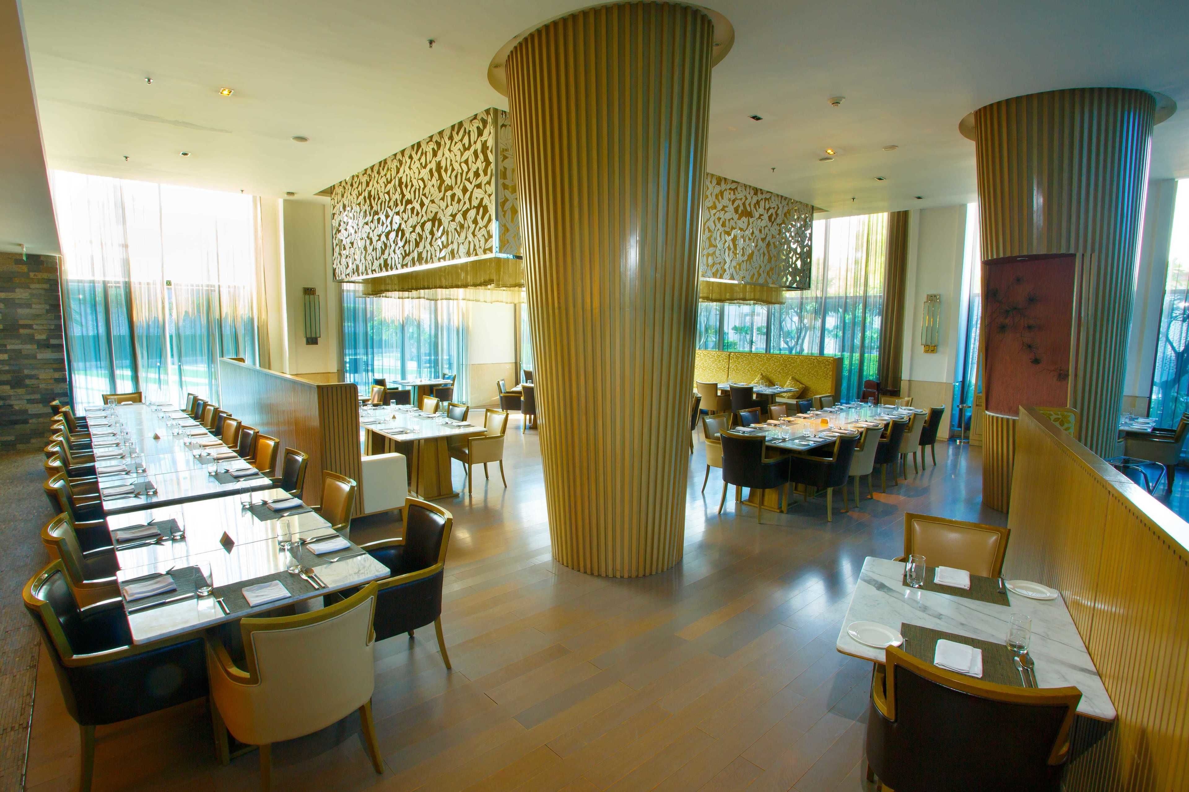 Un vaste espace dédié à la salle à manger, avec de grandes tables et des chaises hautes, de larges fenêtres et des colonnes décoratives.