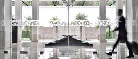Un vestíbulo moderno con piso reflectante, una escalera central y un panel de vidrio con motivos decorativos.