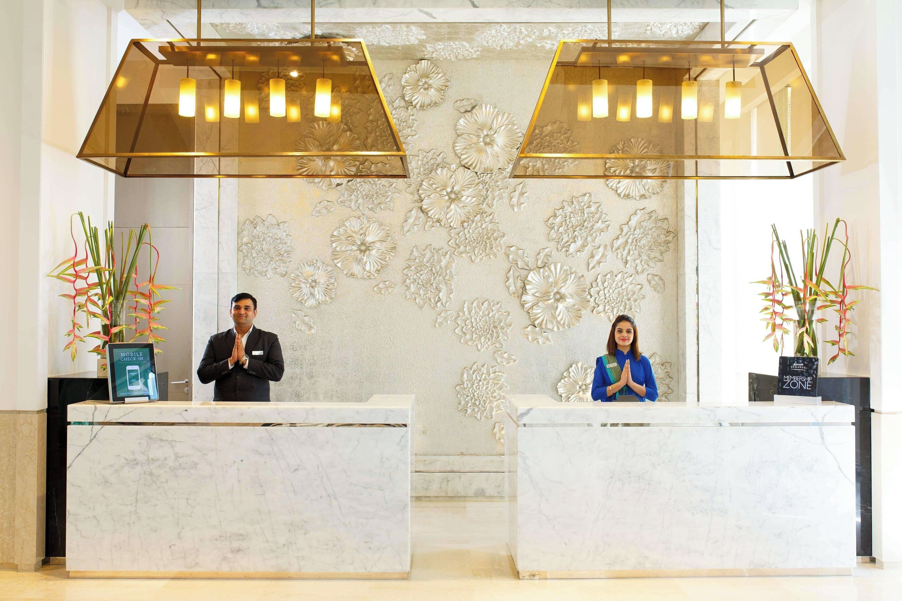 Zona de recepción de hotel con mostradores de mármol, decoración floral en la pared e iluminación colgante moderna.